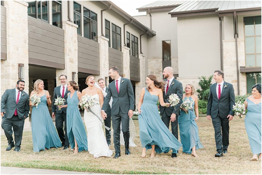 Bridesmaids in dusty blue dress and groomsmen in rust ties walking in front of Grace Bible Church in Houston Texas